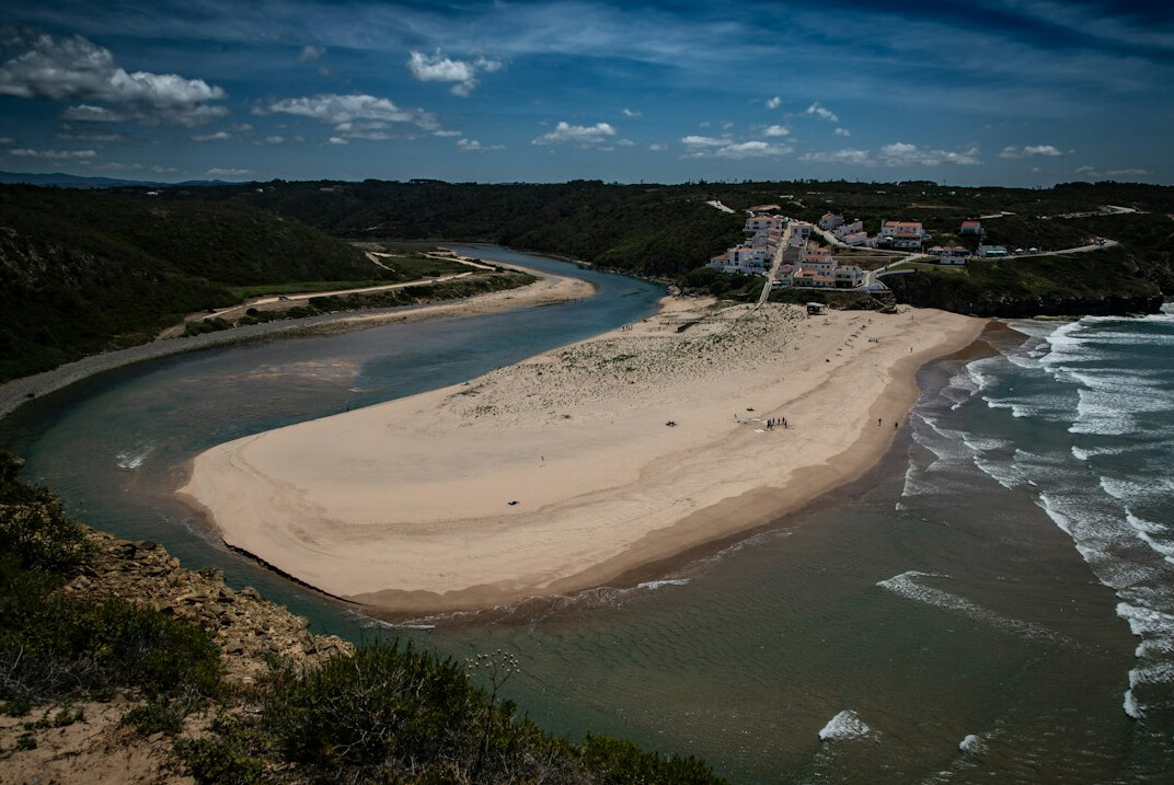 Wooden bridge crossing a calm river mouth surrounded by sand dunes