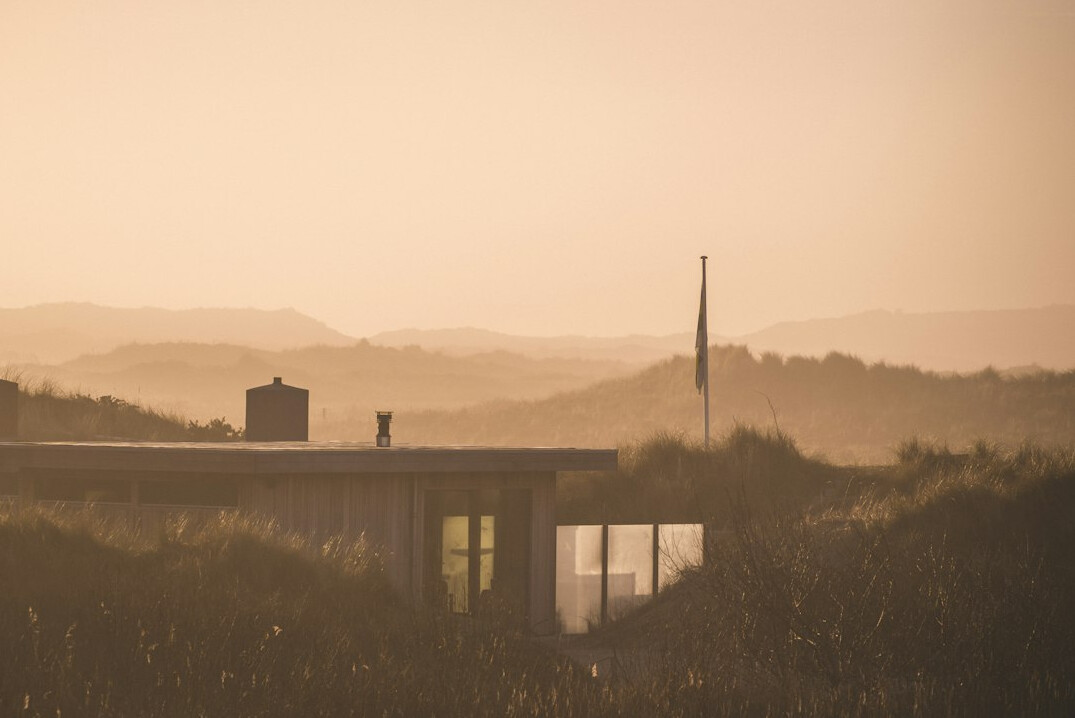 Modern minimalist beach house with large glass windows and wooden deck overlooking dunes